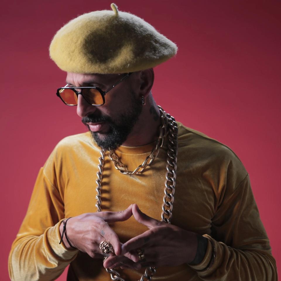 DanniG on a red background wearing a yellow beret and yellow velvet shirt and gold chains