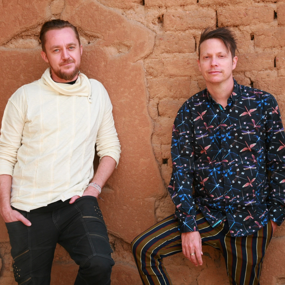 Two white men on a brick background smiling at the camera